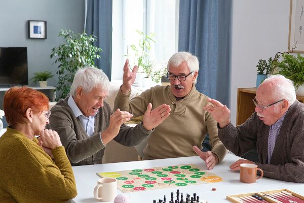 shironosov_iStock-1357526025 1 Seniorin und 3 Senioren spielen ein Brettspiel