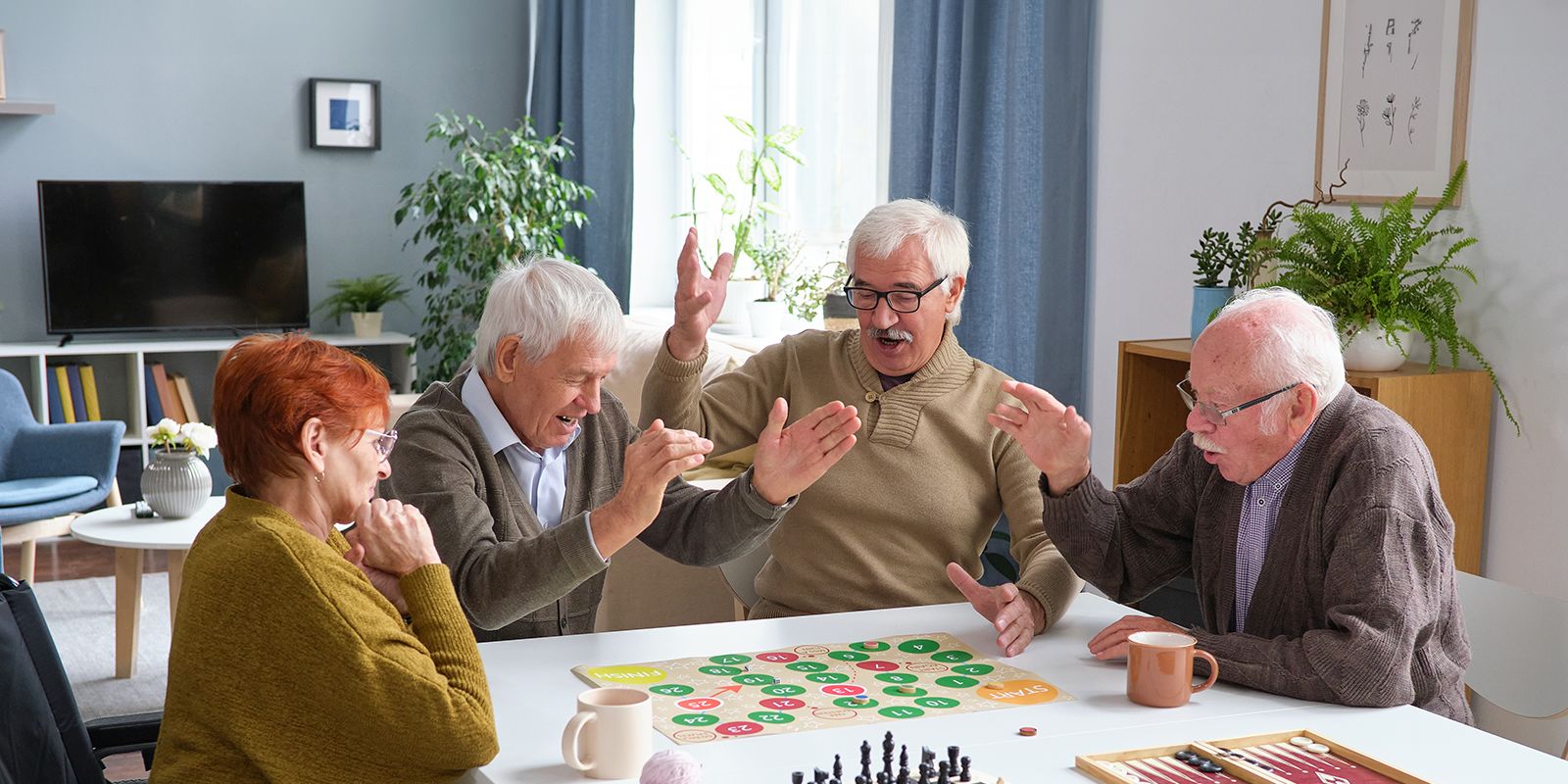 shironosov_iStock-1357526025 1 Seniorin und 3 Senioren spielen ein Brettspiel